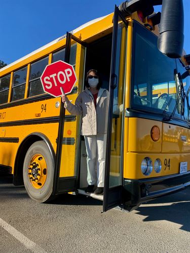 yellow school bus with masked driver holding stop sign